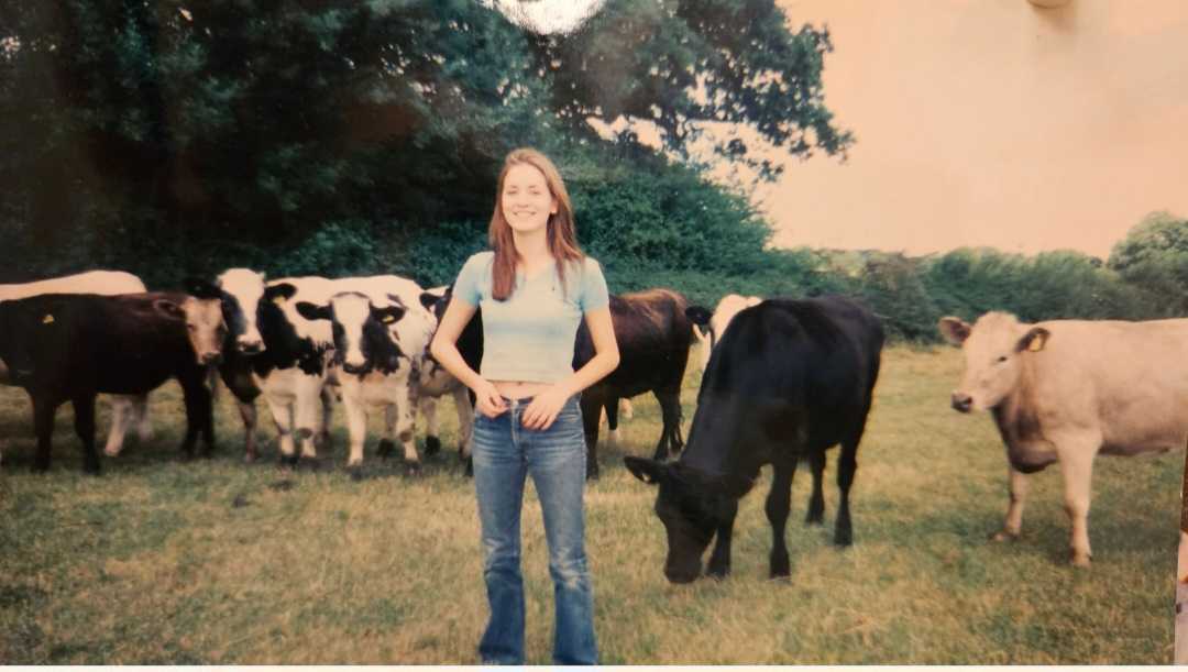 Kelly on the farm, standing among cattle in soft afternoon light